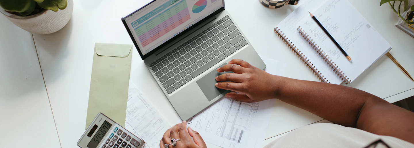 A person working at a laptop with financial reports and a calculator on the desk