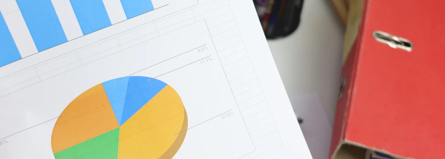 Printed bar and pie charts on a desk beside a red lever arch folder