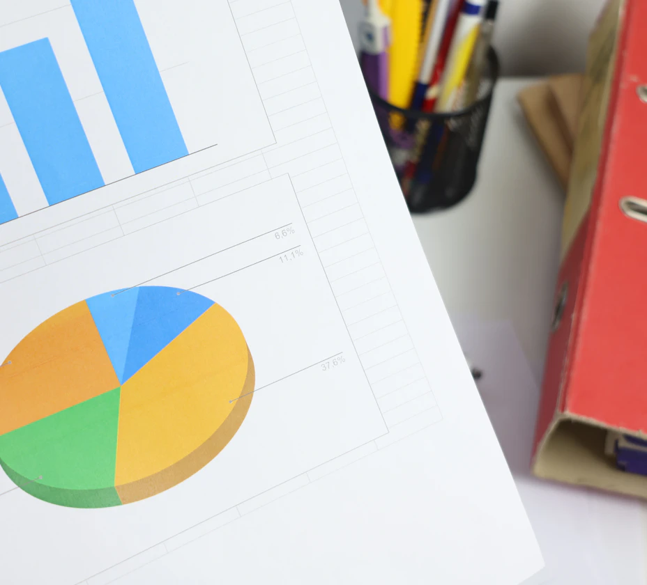 Printed bar and pie charts on a desk beside a red lever arch folder