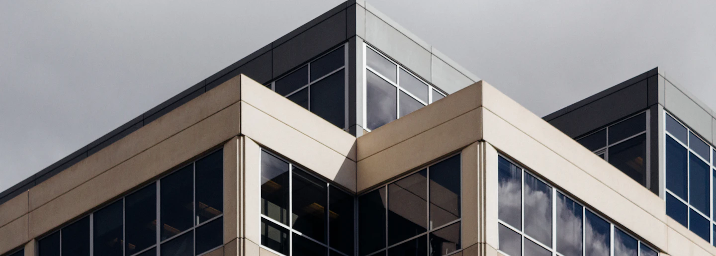 The corner of a modern glass and stone office building against a grey sky