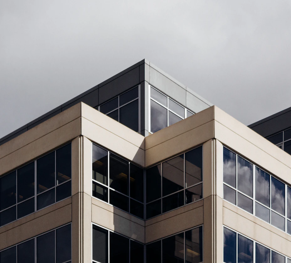The corner of a modern glass and stone office building against a grey sky