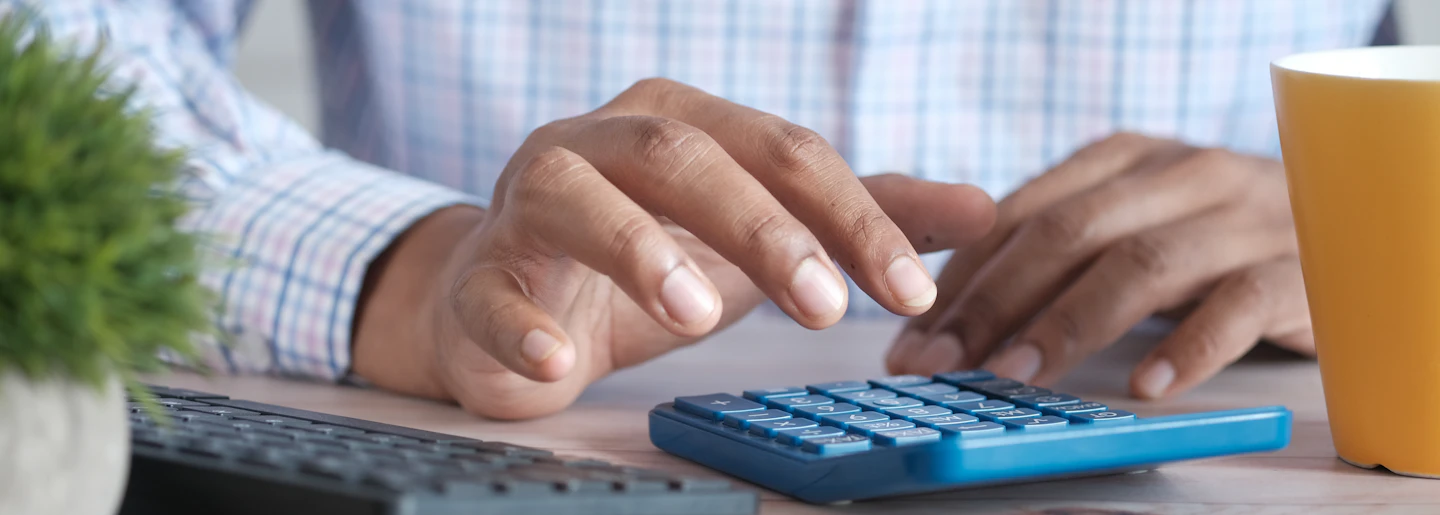 Hands using a calculator next to a keyboard on a desk