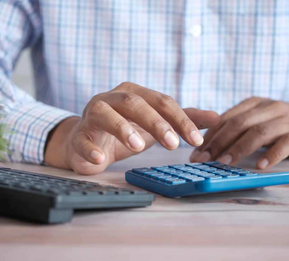 Hands using a calculator next to a keyboard on a desk