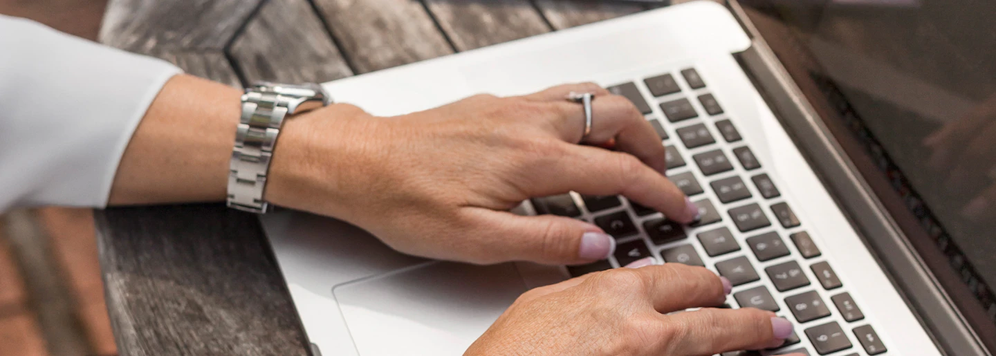 Hands typing on a laptop keyboard beside an open notebook