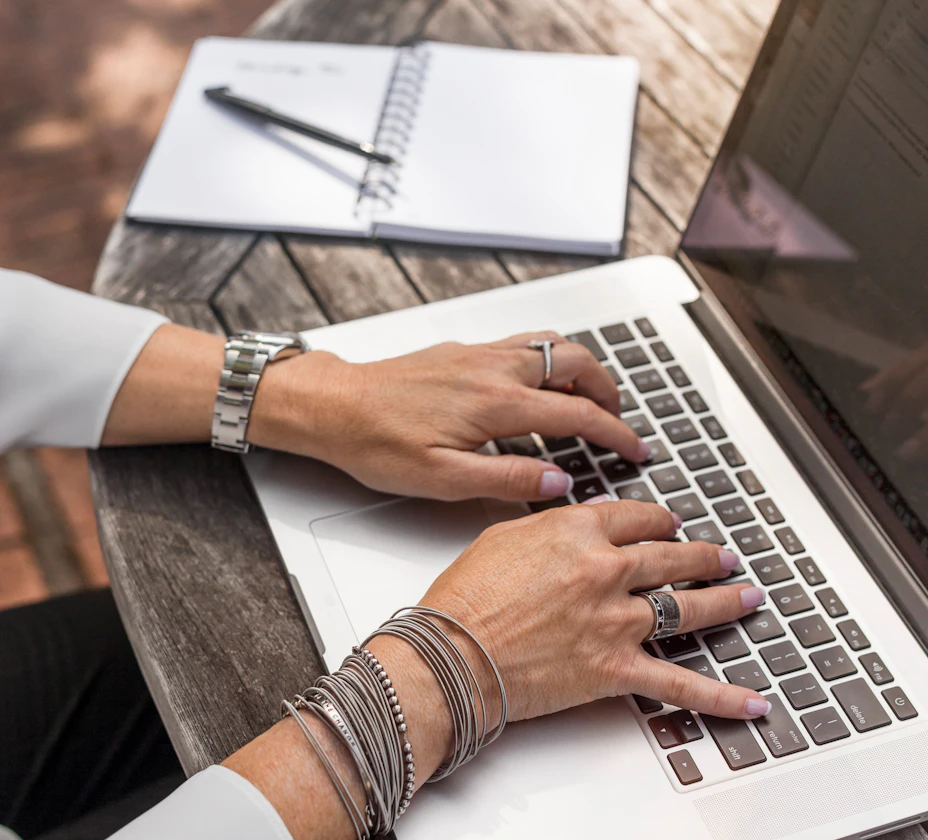 Hands typing on a laptop keyboard beside an open notebook