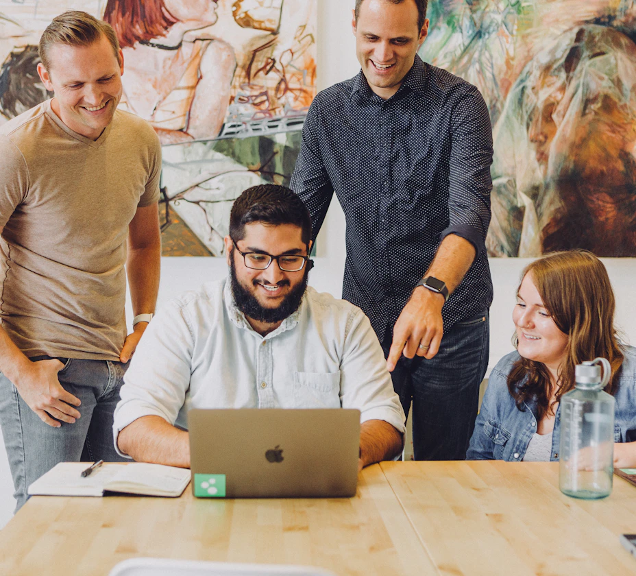 A group of young colleagues gathered around a laptop in an office