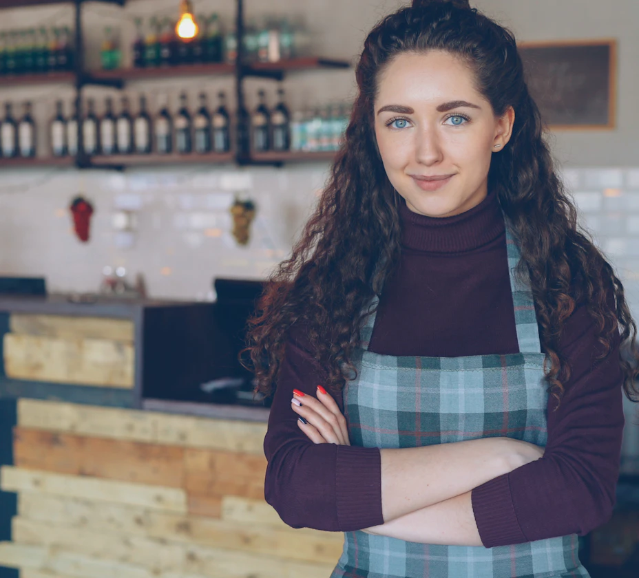 Small business owner in an apron standing behind the counter of her shop